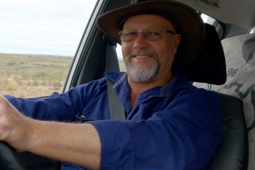 Man wearing cowboy hat driving and smiling. 