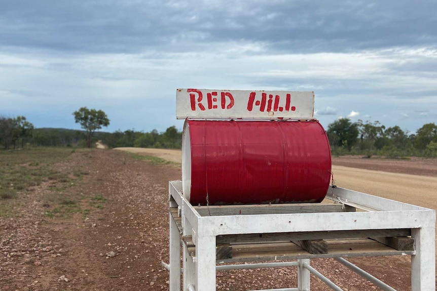A bright red mail box on a remote property with the name "Red Hill" attached to it.
