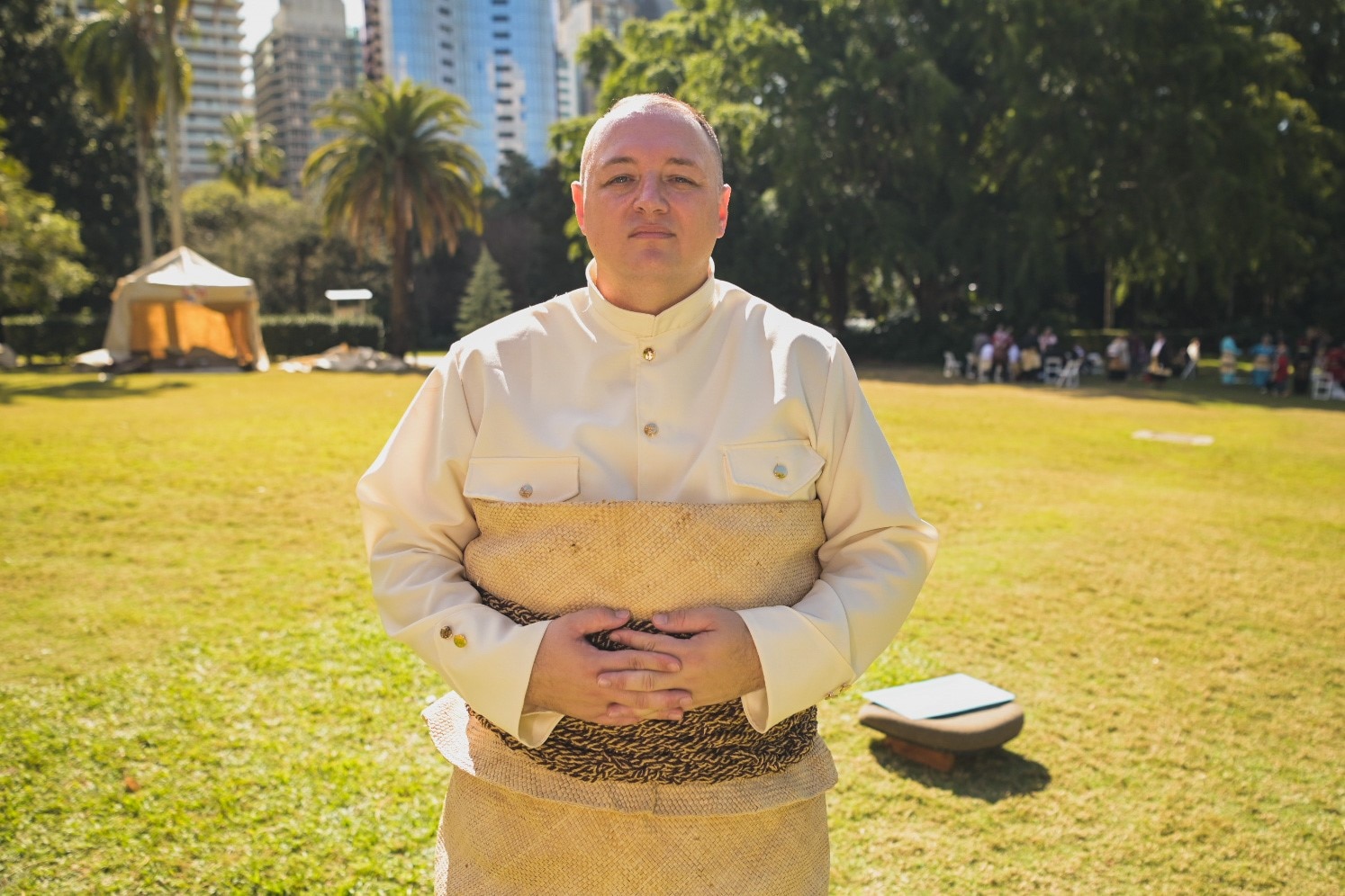 Sulieni Layt with hands interlaced in a green park in traditional Tongan clothing.