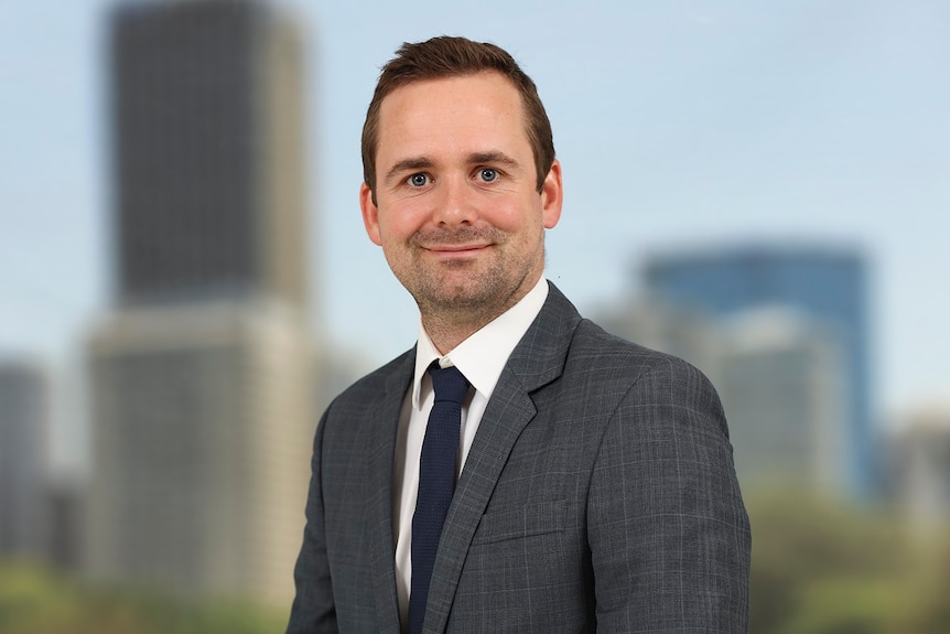 Kristian Kolding, wearing a suit looks ahead with a smile on his face.