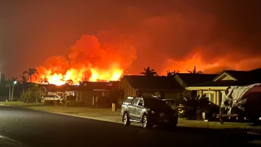 flames light up night sky behind houses
