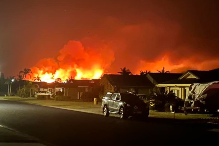 flames light up night sky behind houses