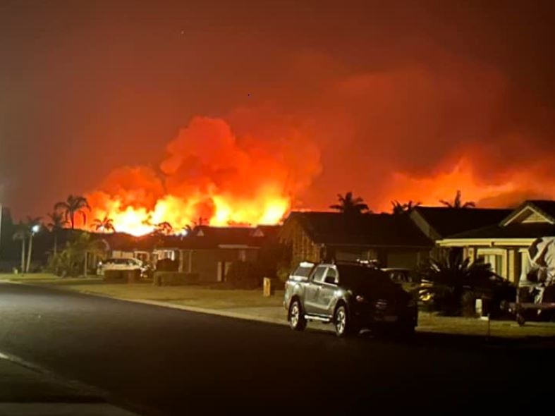 flames light up night sky behind houses