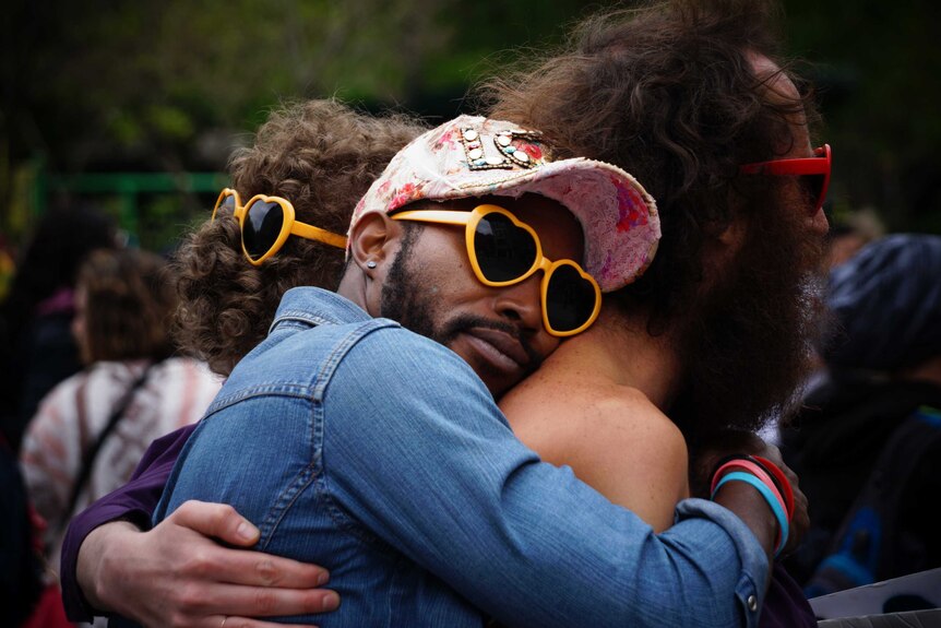 Man hugs another man while wearing heart-shaped sunglasses and a cap to depict how to choose the best sunscreen.