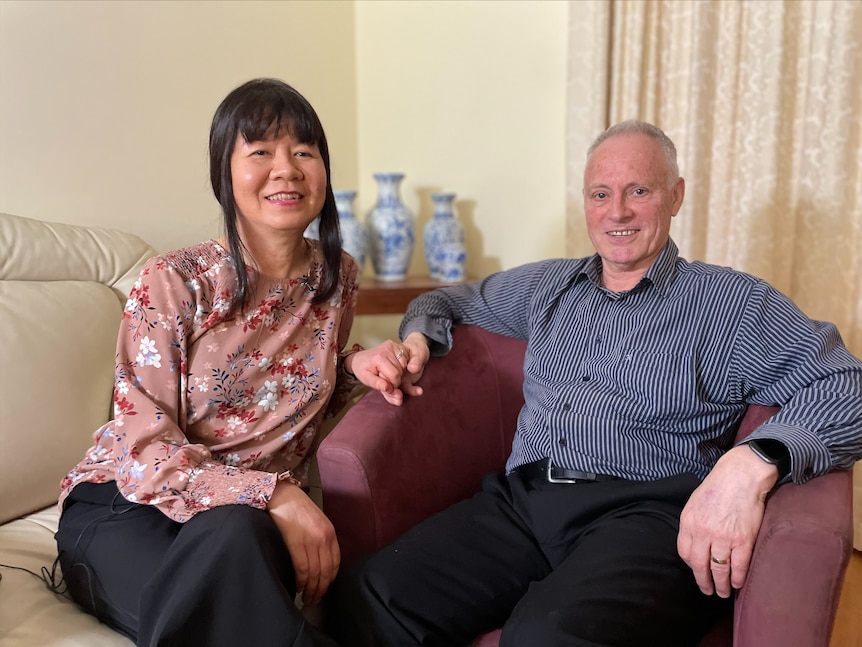 一名身穿深蓝色衬衫和黑色裤子的男子握着一名女子的手，两人坐在休息室的沙发上。
