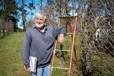 David Pickering standing next to apple trees in paddock, leaning on ladder