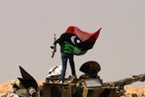 A Libyan rebel stands on a burnt out tank and waves the rebellion flag