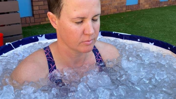 Joy Symons sitting in a round tub with her eyes closed and ice up to her shoulders.