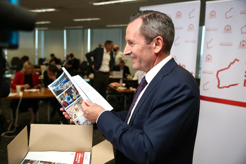 A side-profile photo of Mark McGowan flicking through budget papers.