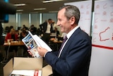 A side-profile photo of Mark McGowan flicking through budget papers.