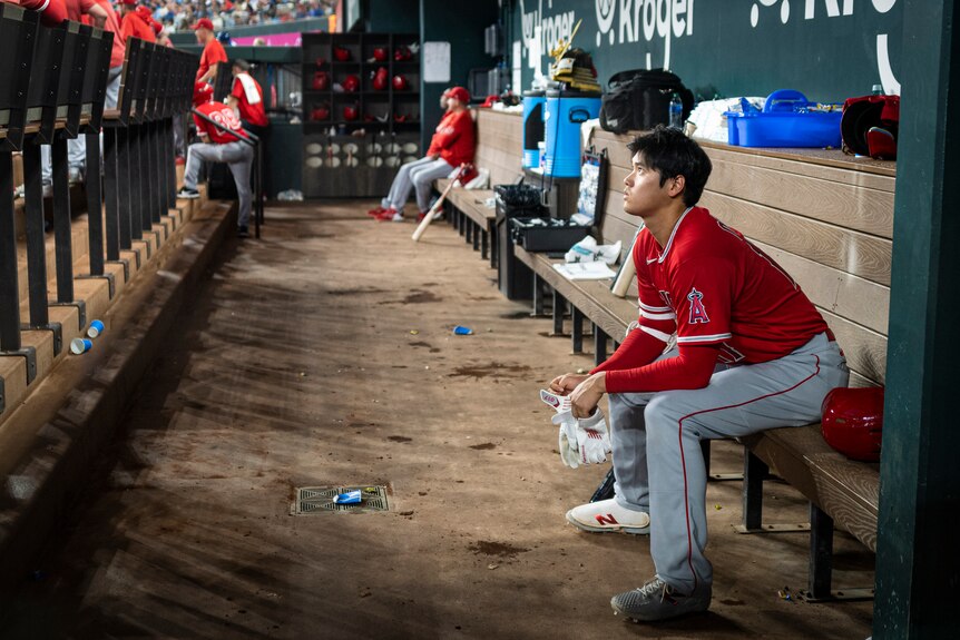 A baseball player sits alone in the dugout
