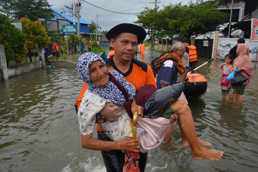 A young man carries an elderly woman through floodwaters