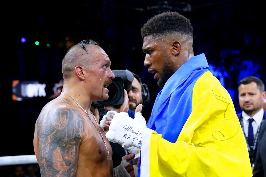 Oleksandr Usyk, bare chested, and Anthony Joshua, draped in a Ukraine flag, talk face to face