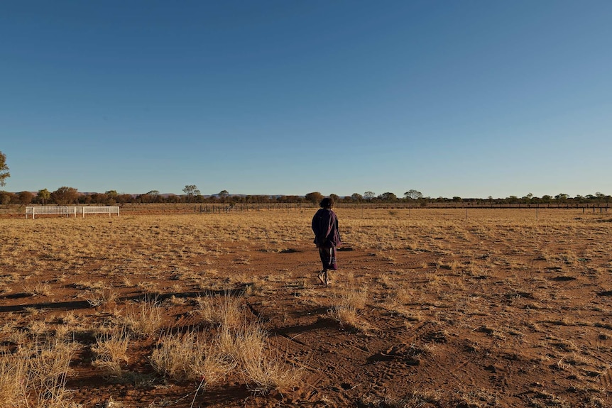 Anne Lane walks away from her daughter's grave across a patchy field in Haasts Bluff.