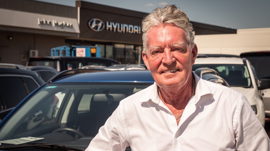 Man in white shirt stands in front of cars in car yard