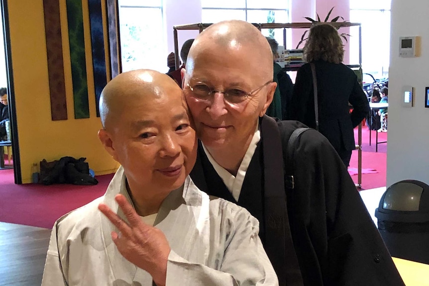 Buddhist nun with light coloured robes and peace sign poses for photo next to Buddhist in dark robes.