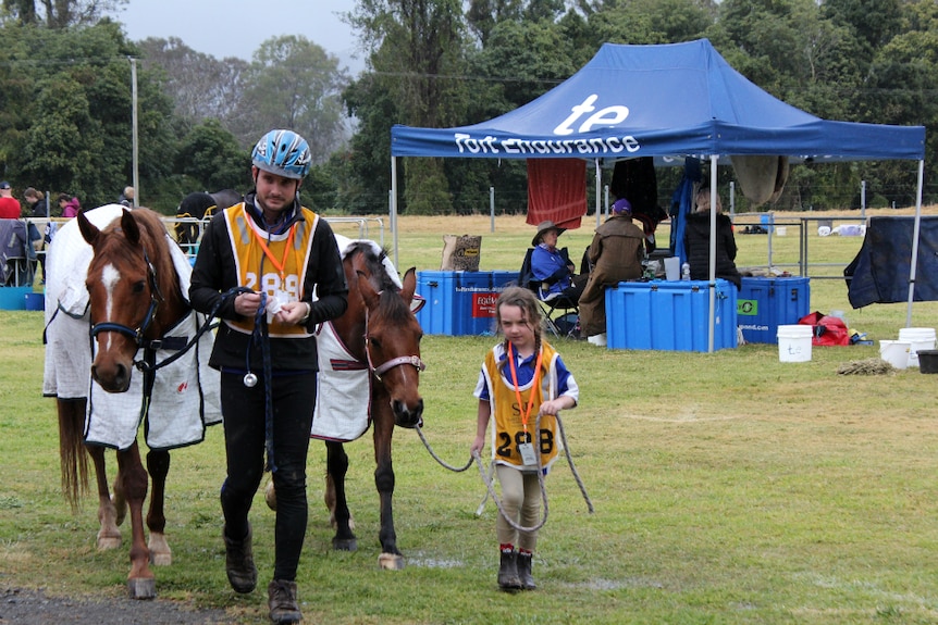 A dad and his five-year-old daughter lead their horses.