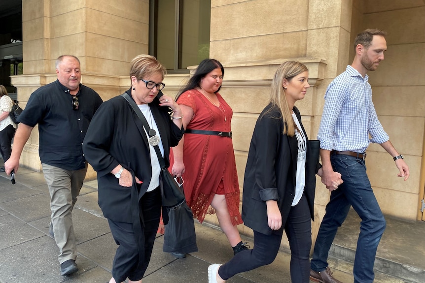Five people walk outside a beige court building