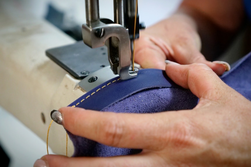 A close up of a woman's hands holding leather that is being stitched on a machine