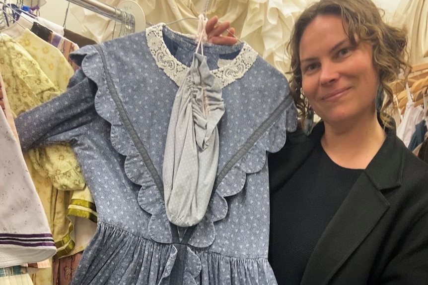 A woman holds an 1850s blue dress 