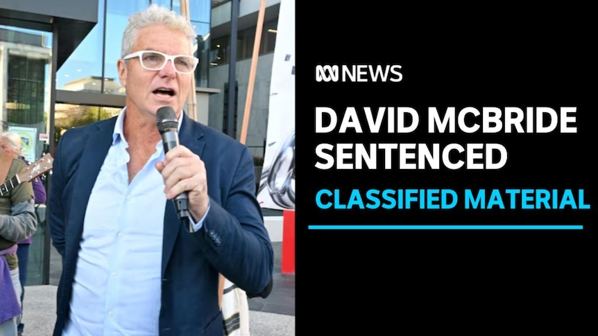 David McBride Sentenced, Classified Material: A man with white-rimmed glasses speaks into a microphone he's holding.