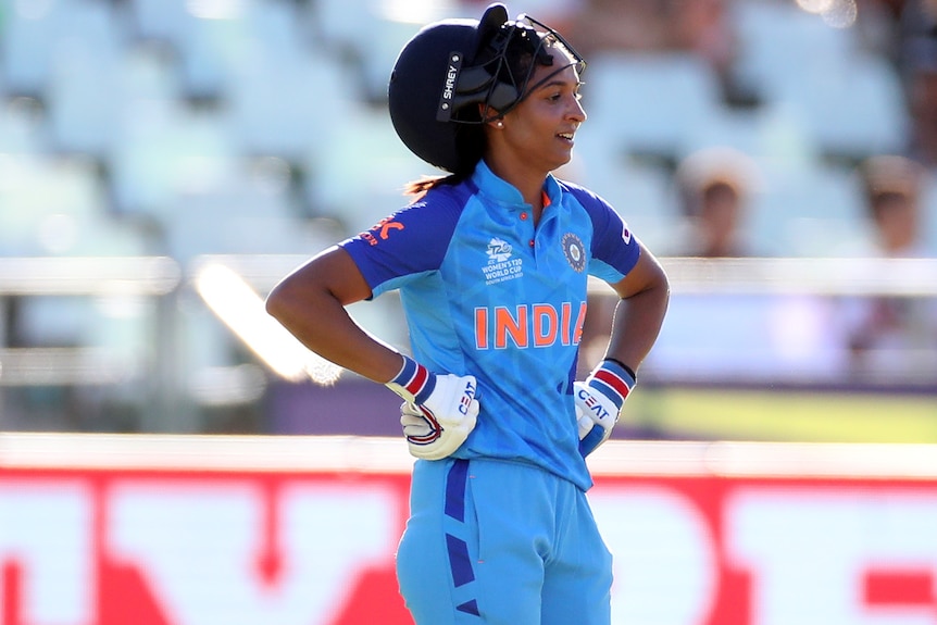 A cricketer stands with hands on her hips.