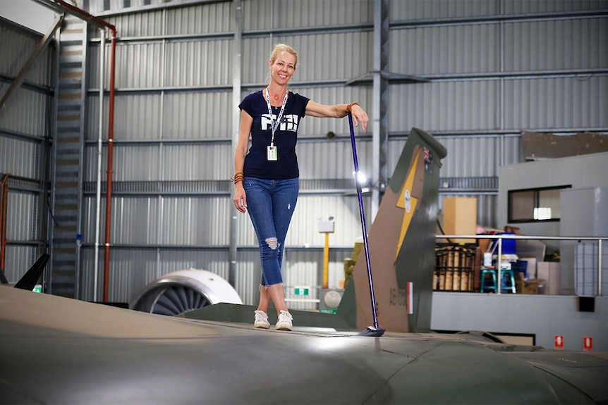 Melinda Andersson leans on a broom on top of the F-111 at HARS.