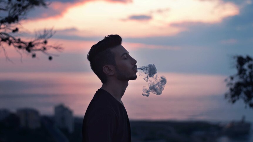 A man blow smoke in front of a sunset