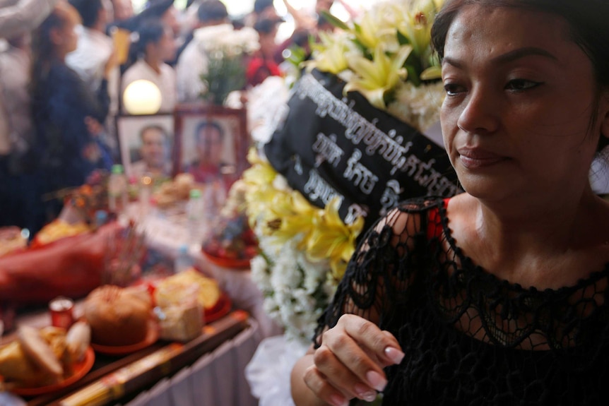 Bou Rachana attends her husband's funeral, wearing black and surrounded by flowers.
