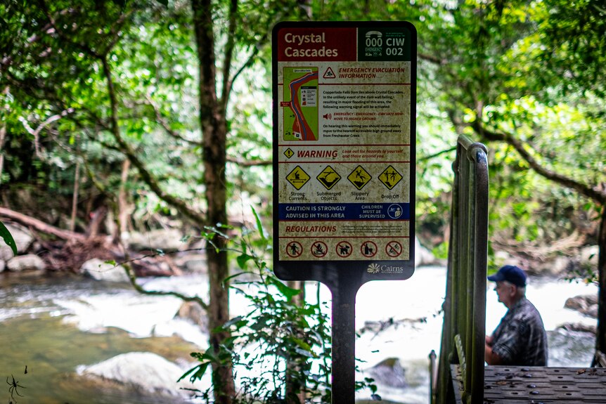 Warning sign covered in moss at a tropical creek.