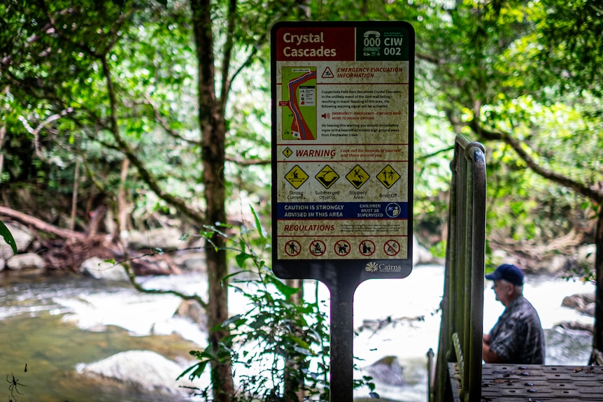Warning sign covered in moss at a tropical creek.