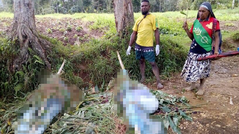A man and a woman stand by the bodies of women and children wrapped up after they were killed in Papua New Guinea