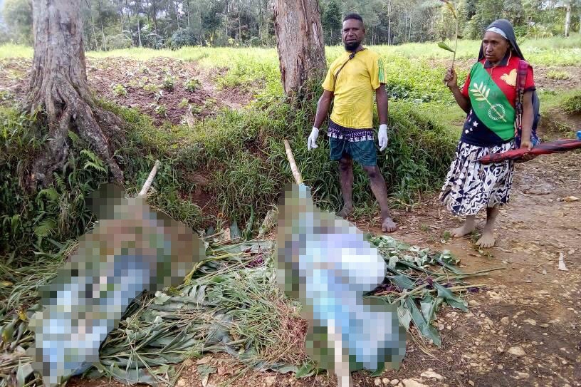 A man and a woman stand by the bodies of women and children wrapped up after they were killed in Papua New Guinea