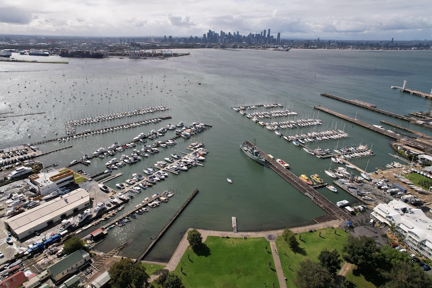 A drone shot of boats docked at several piers with the city of melbourne in the distant background. 