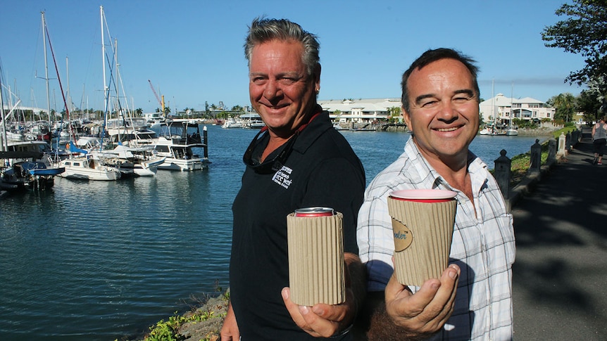 Two men holding cardboard stubby coolers