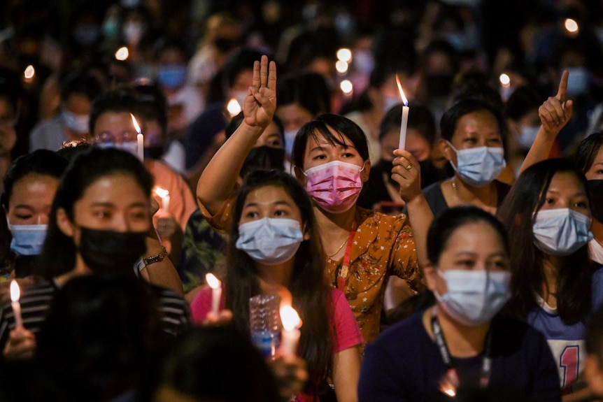 Protesters hold candles and some flash a three-fingered salute.