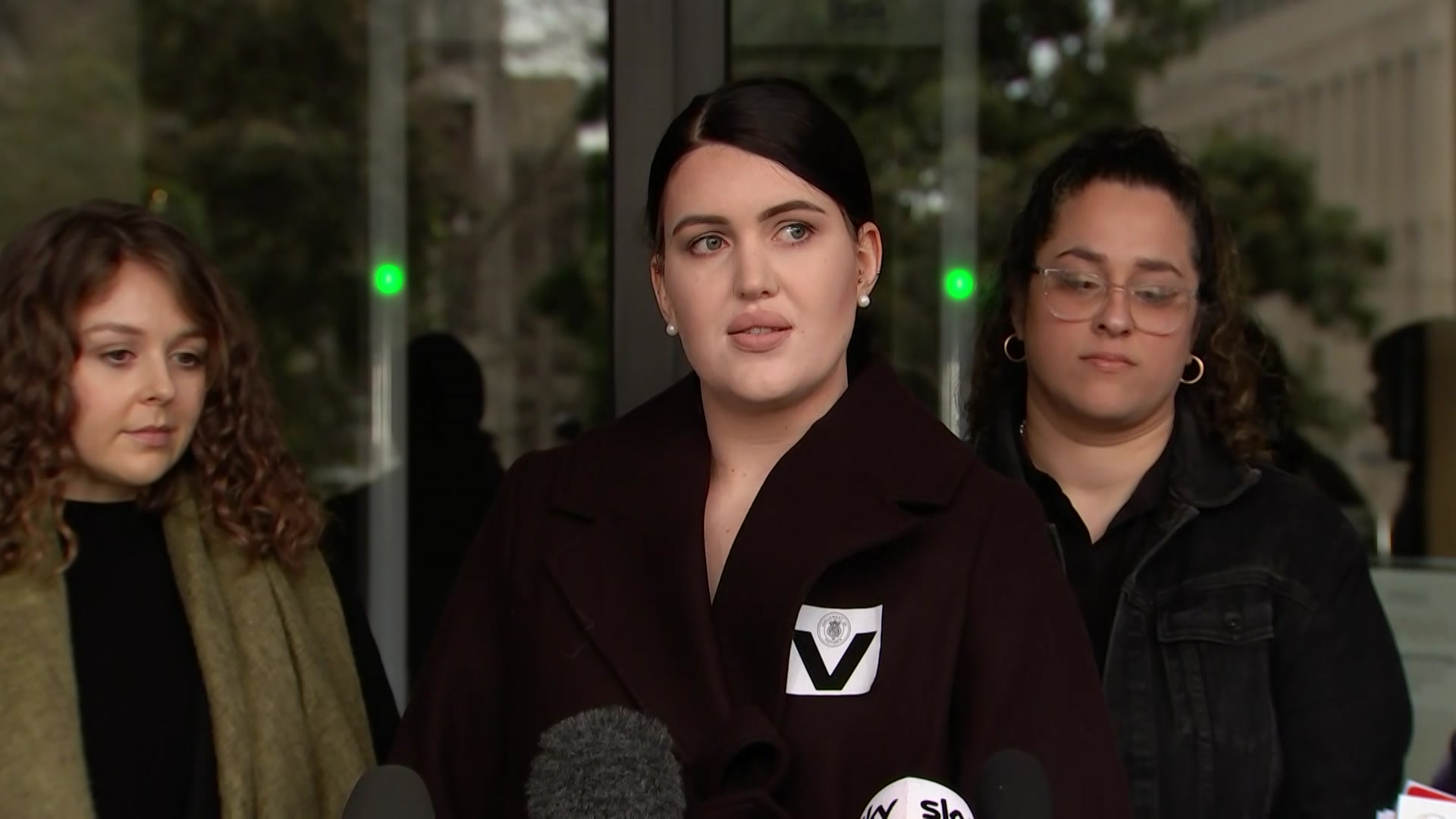 A woman with dark hair speaking in front of microphones.
