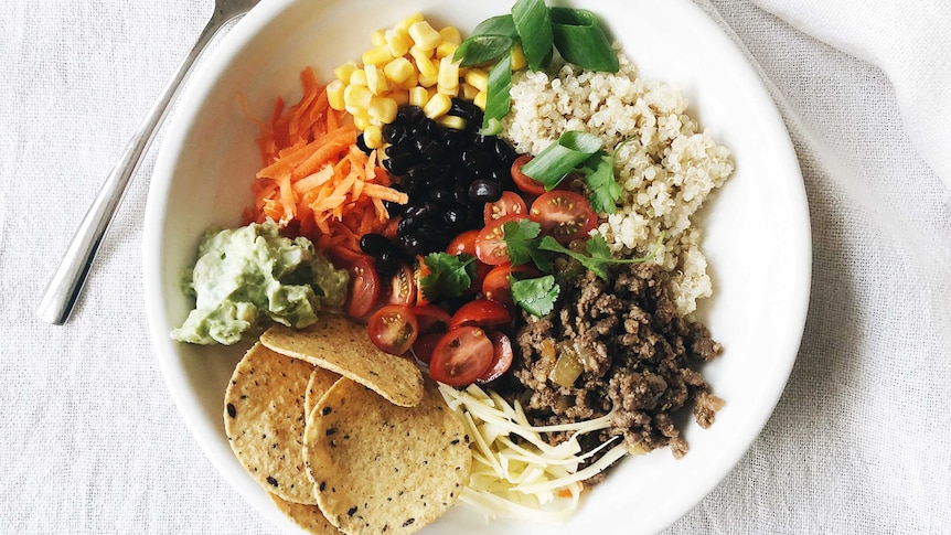 Taco bowl with carrots, corn, quinoa, spiced meat, cherry tomatoes, cheese, corn chips, guacamole and beans from our recipe
