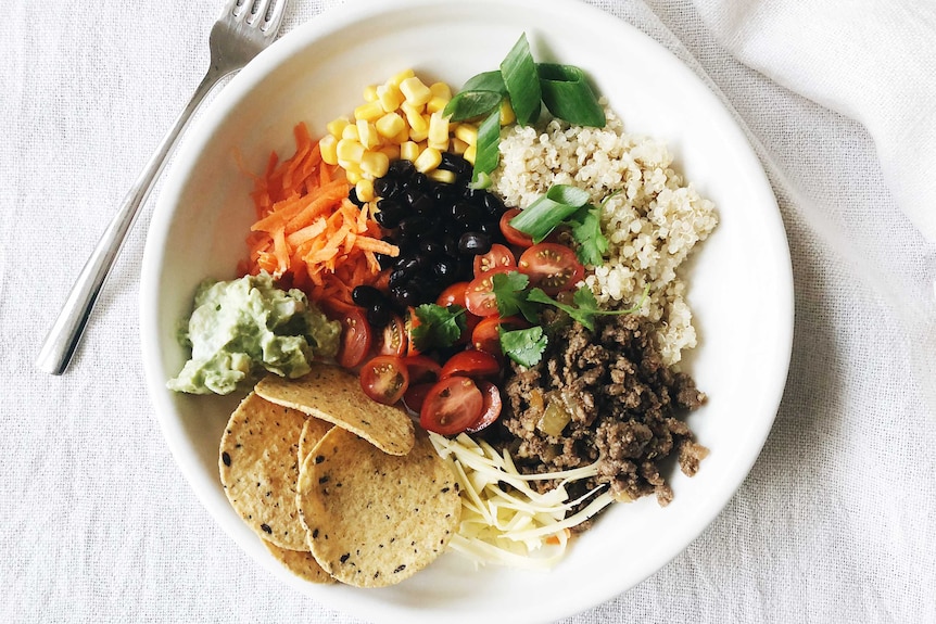 Taco bowl with carrots, corn, quinoa, spiced meat, cherry tomatoes, cheese, corn chips, guacamole and beans from our recipe