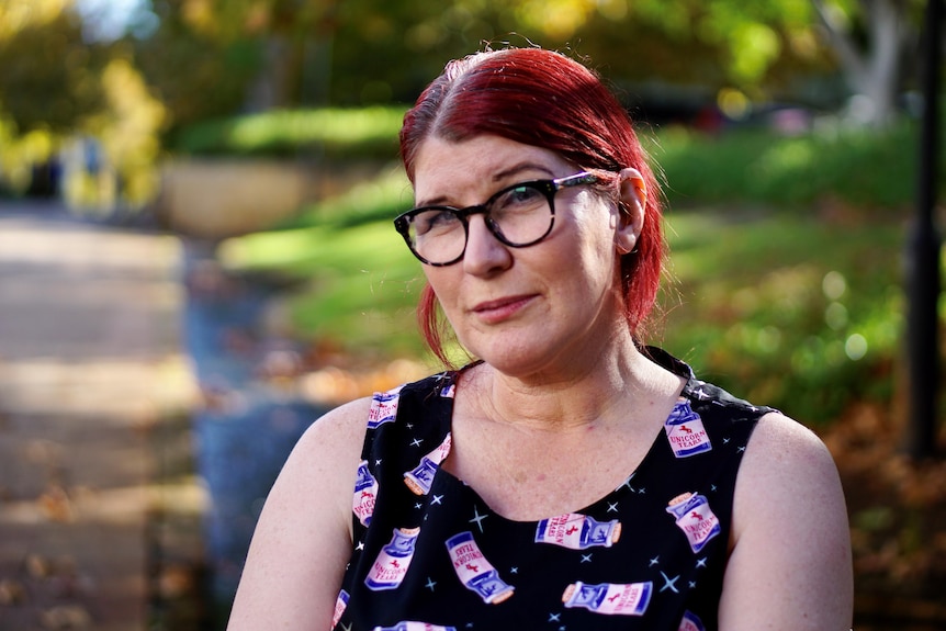 A woman with red hair and glasses is sitting outside.