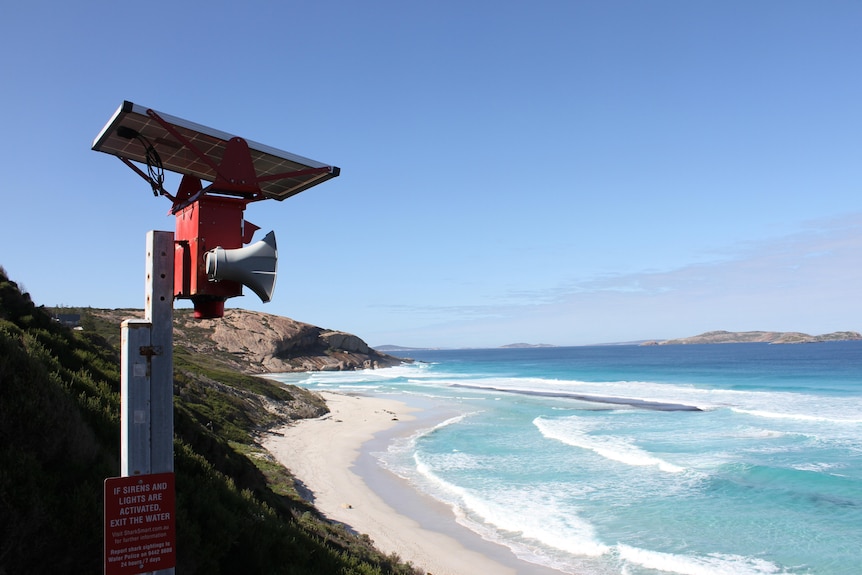 A loudspeaker attached to a red pole stands overlooking a stretch of coast.