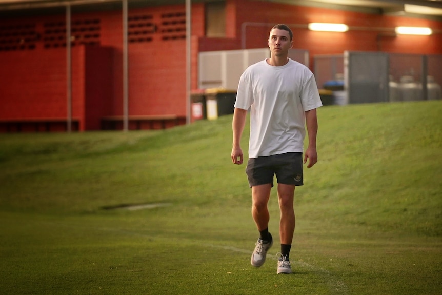 A young man walking on a football field with a building in the background