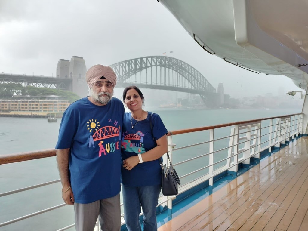 An elderly man in a turban hugs his wife on a boat in front of the Sydney Harbour Bridge