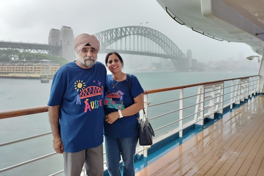 An elderly man in a turban hugs his wife on a boat in front of the Sydney Harbour Bridge