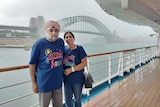 An elderly man in a turban hugs his wife on a boat in front of the Sydney Harbour Bridge