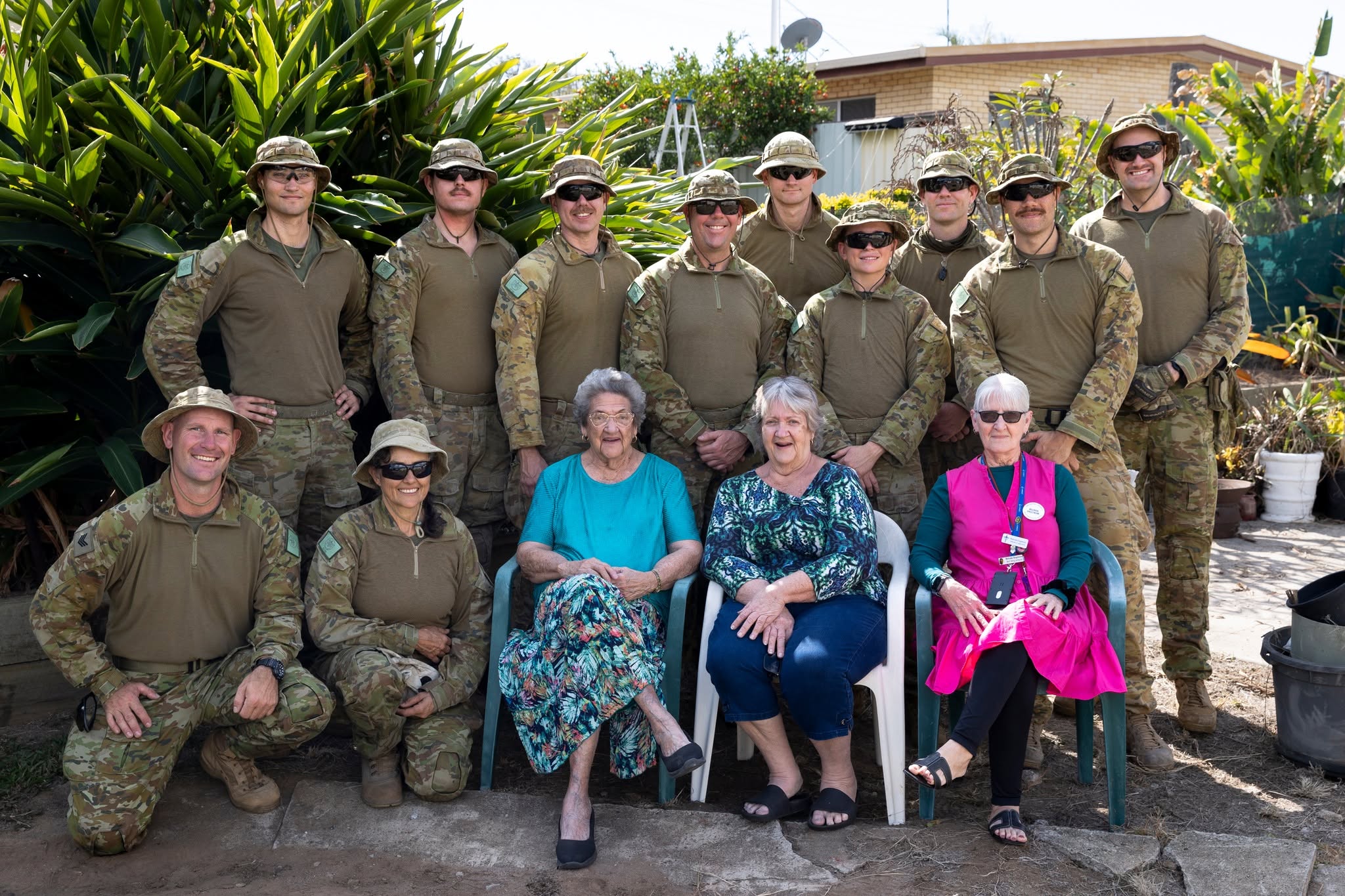 Three mature women sitting smiling with a group of soldiers in army fatigues.