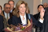 Caroline Kennedy waving while holding a big bunch of flowers 