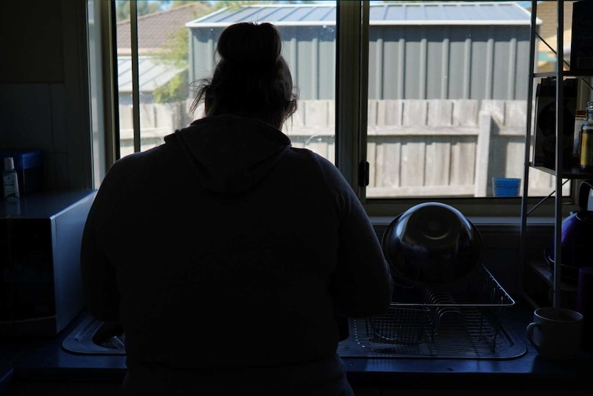 A woman is shown from behind standing at a kitchen sink.