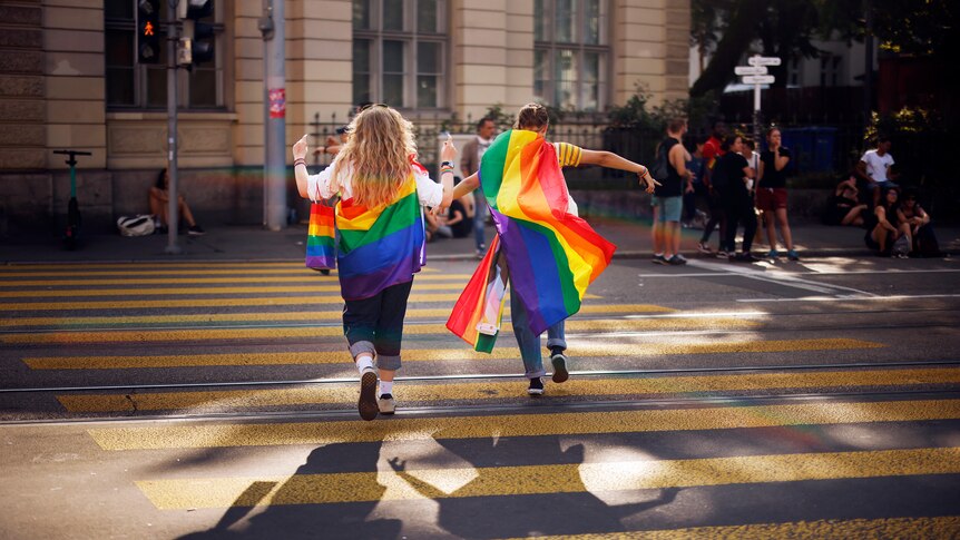 Two people hold a rainbow flag while crossing a street in Zurich