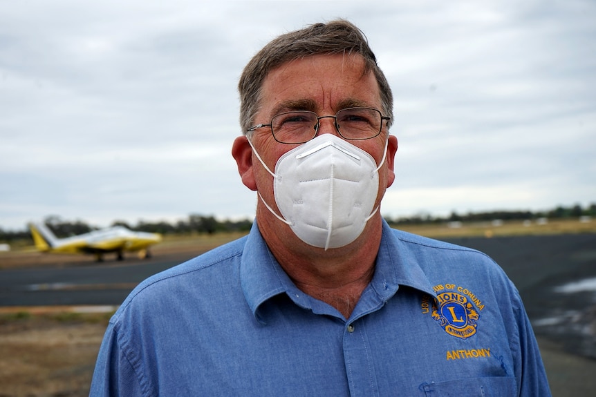 A close up of a man in blue shirt with the Lions' logo, wearing a mask and glasses.